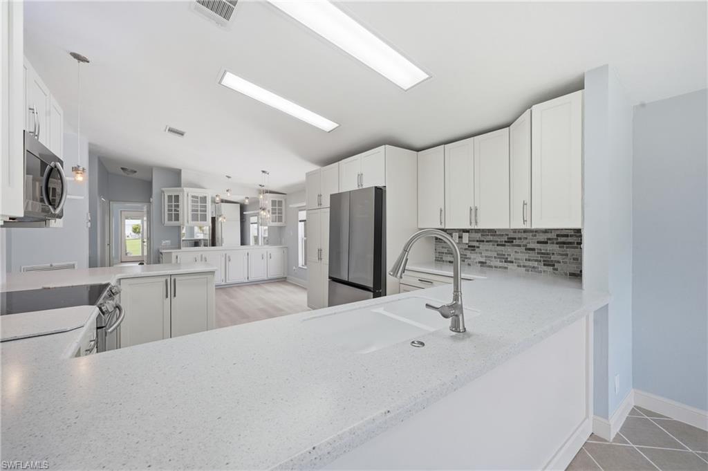 Kitchen featuring white cabinetry, light-toned countertops, stainless steel appliances, and a mosaic tile backsplash