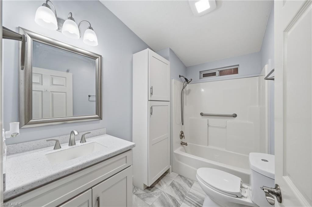 Bathroom featuring a single vanity with stone-finish countertop, framed mirror, and a three-light fixture