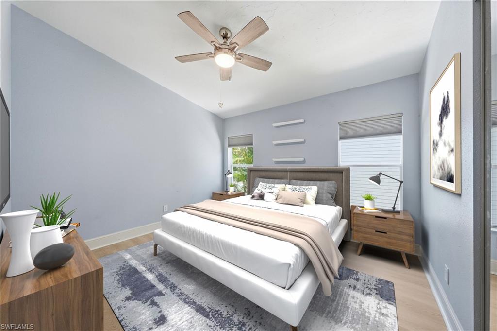 Spacious bedroom featuring light-toned wood-finish flooring, a contemporary ceiling fan, and two windows with blinds