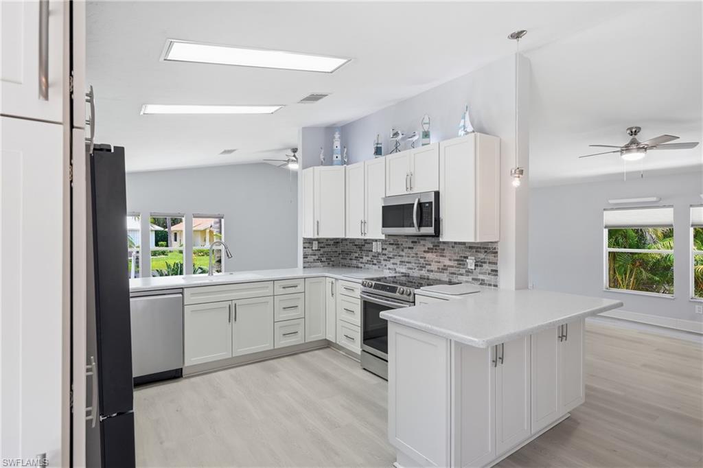 Contemporary kitchen featuring white cabinetry, stainless steel appliances, a mosaic tile backsplash, a countertop island, and light wood-finish flooring