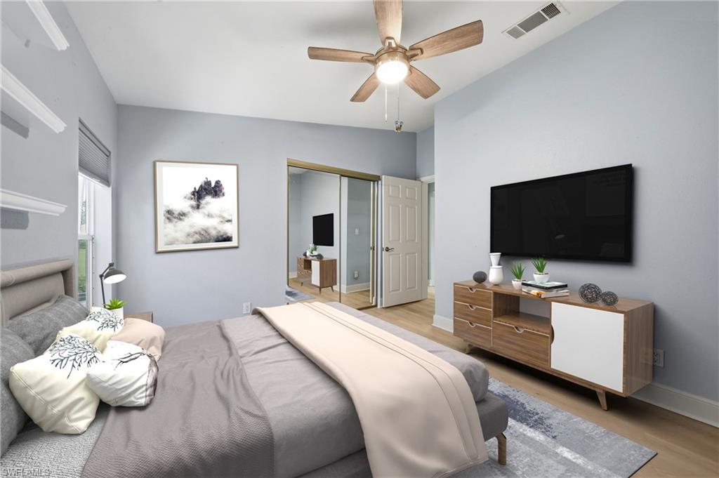 Spacious bedroom featuring light blue walls, a ceiling fan with light fixture, wood-finish flooring, and a mirrored closet door