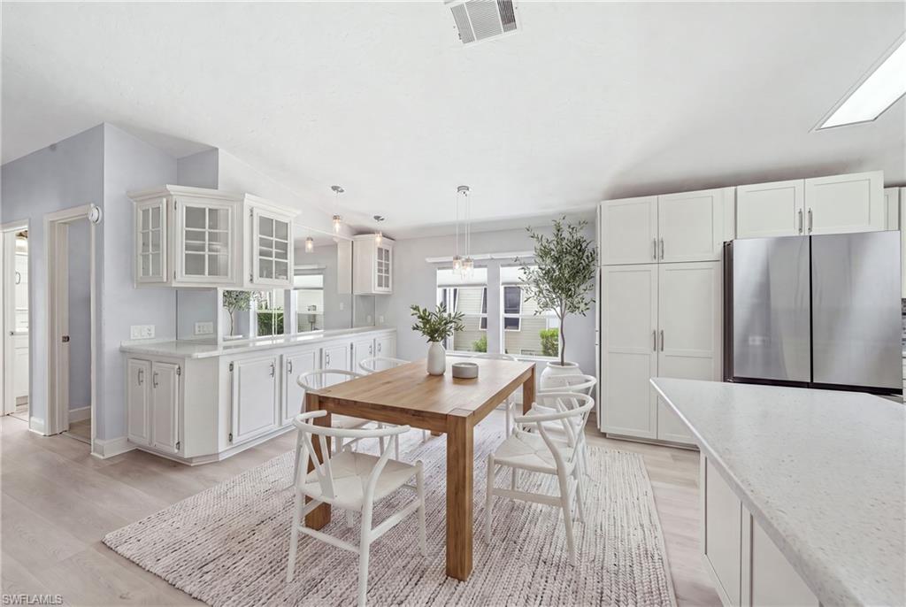 Light-filled kitchen and dining area featuring white cabinetry, light-tone wood-finish flooring, and a skylight