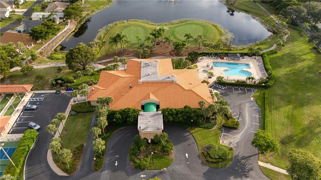 Clubhouse building with orange tile roof, adjacent to a resort-style swimming pool, two golf greens, and a tennis court