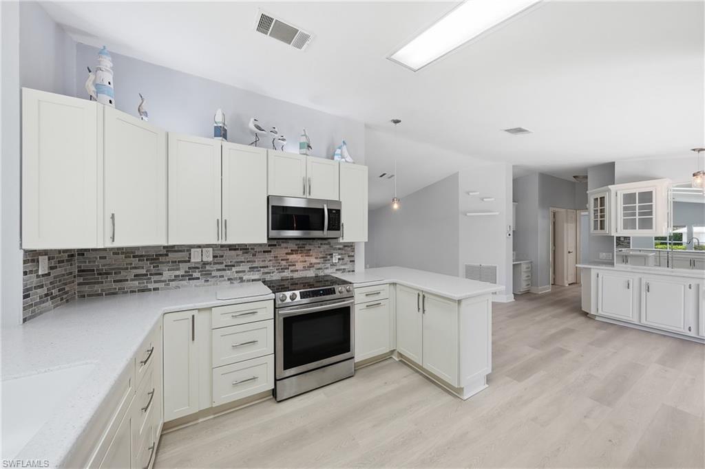 Modern kitchen featuring white cabinetry, stainless steel appliances, light-toned countertops, and a mosaic tile backsplash