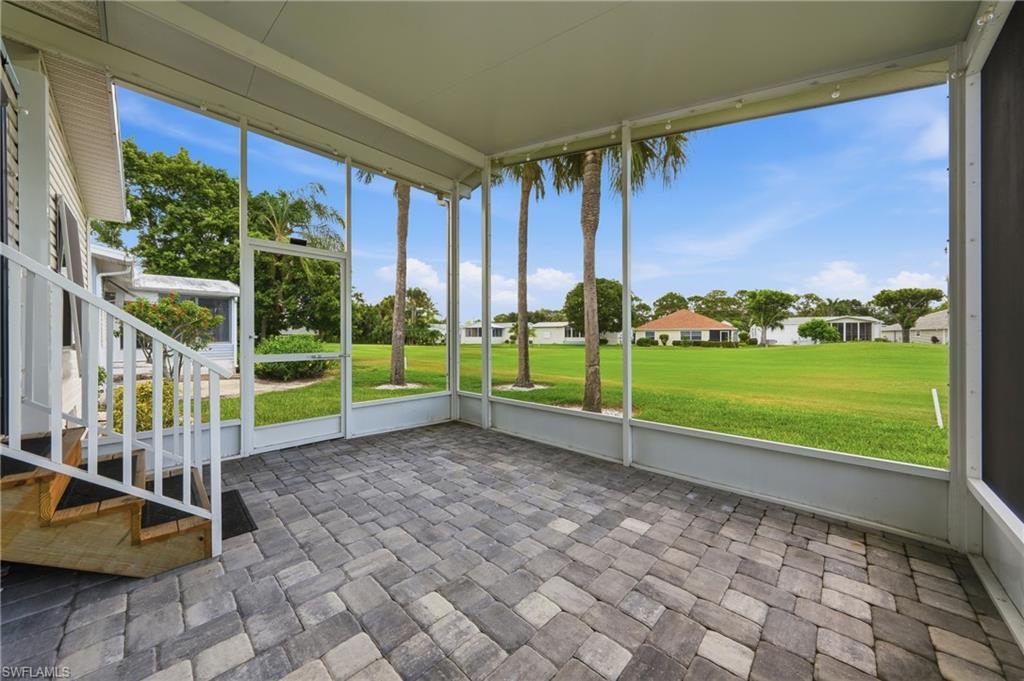 Screened patio featuring paver flooring, white railings, and a wide outdoor expanse with palm trees and manicured lawns