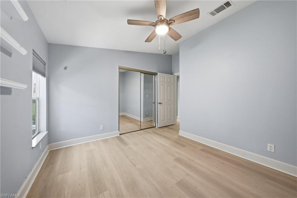 Bright room featuring wood-finish flooring, a ceiling fan with integrated lighting, mirrored sliding closet doors, and a window with blinds