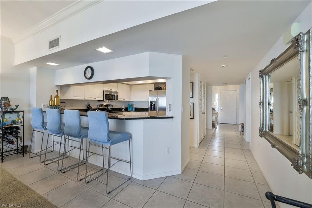 Kitchen featuring light tile patterned flooring, dark countertops, stainless steel appliances, a peninsula, and ornamental molding