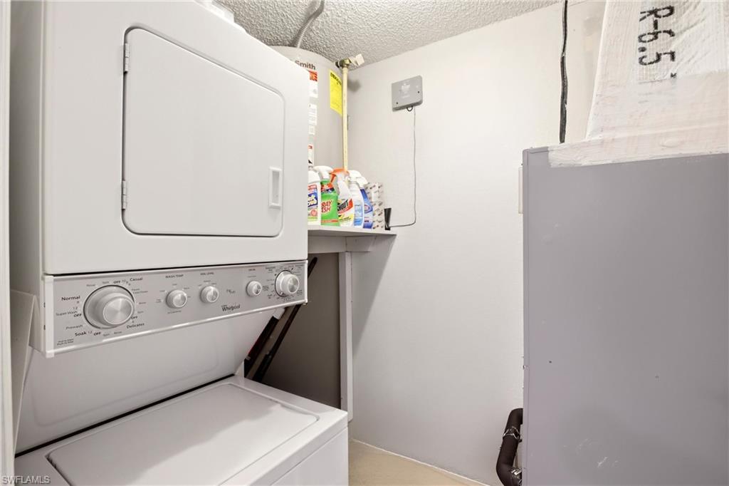 Laundry area featuring a textured ceiling, stacked washer / drying machine, water heater, and heating unit