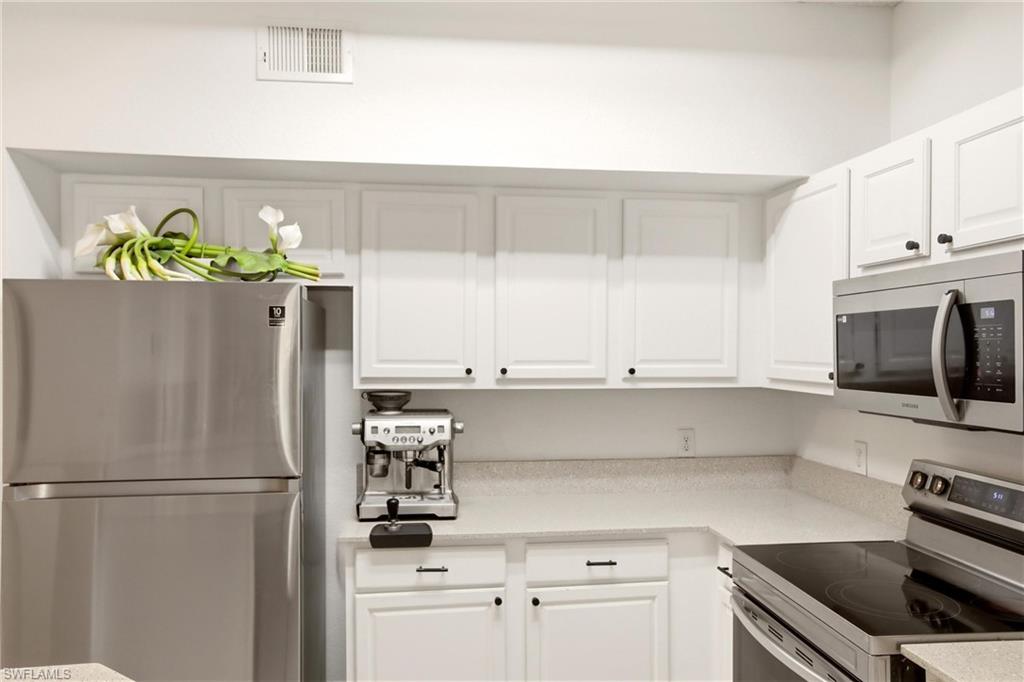 Kitchen with stainless steel appliances, white cabinetry, and light stone countertops