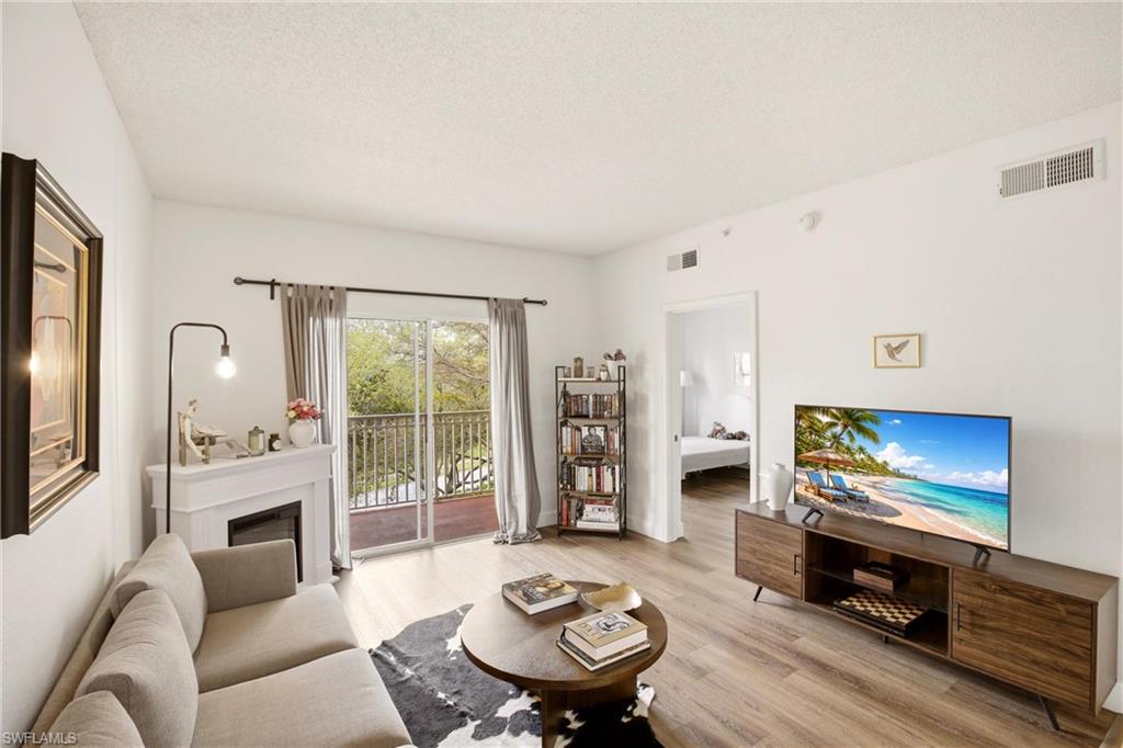 Living room with light wood-style floors, a glass covered fireplace, and a textured ceiling