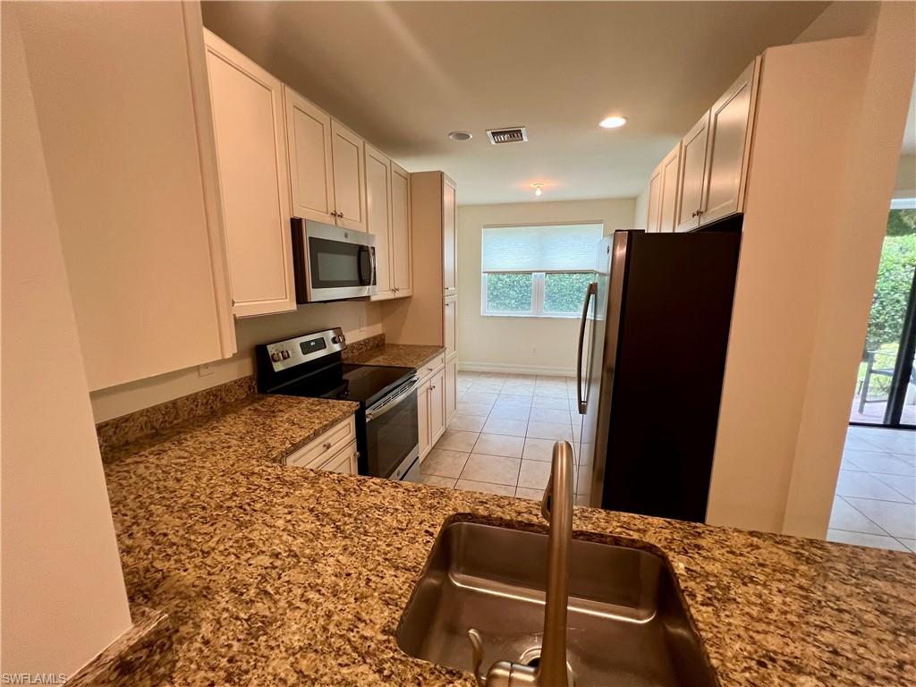 Kitchen with light tile patterned flooring, white cabinetry, and stainless steel appliances