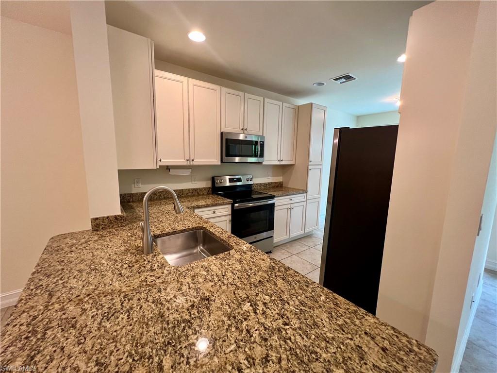 Kitchen featuring white cabinetry, stainless steel appliances, sink, dark stone countertops, and light tile patterned floors