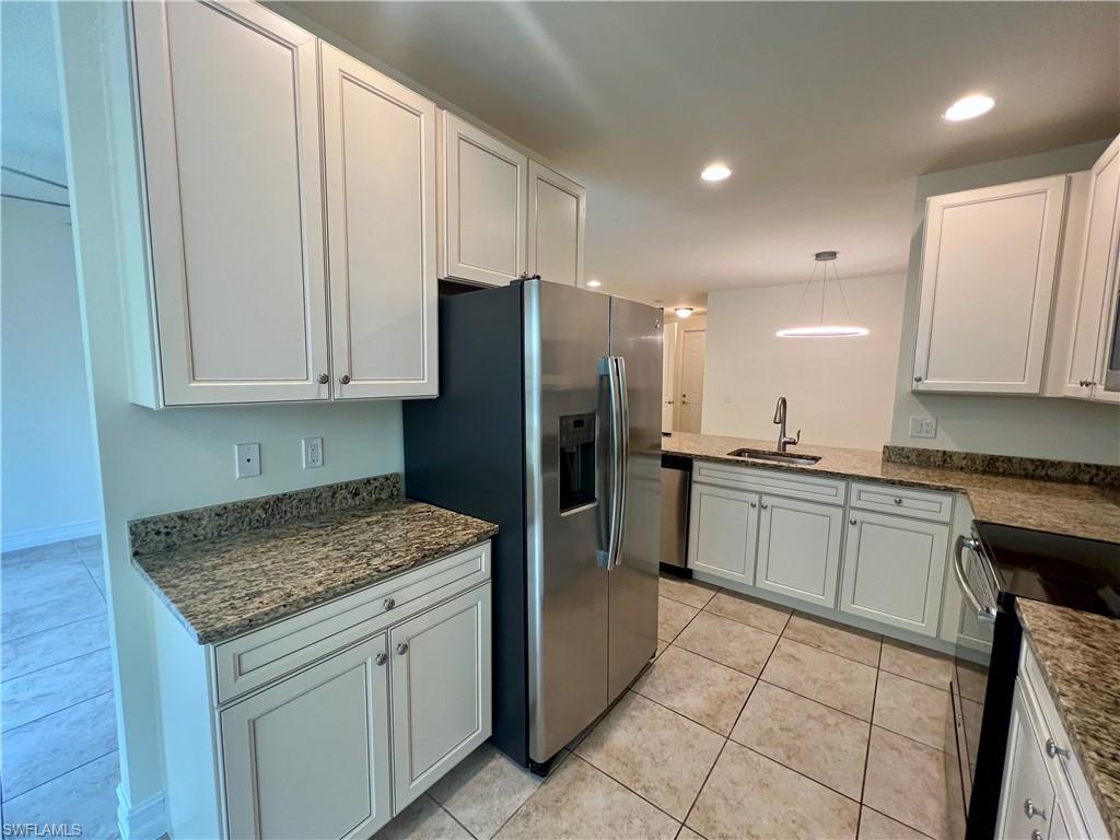 Kitchen featuring light tile patterned flooring, decorative light fixtures, white cabinetry, sink, and appliances with stainless steel finishes