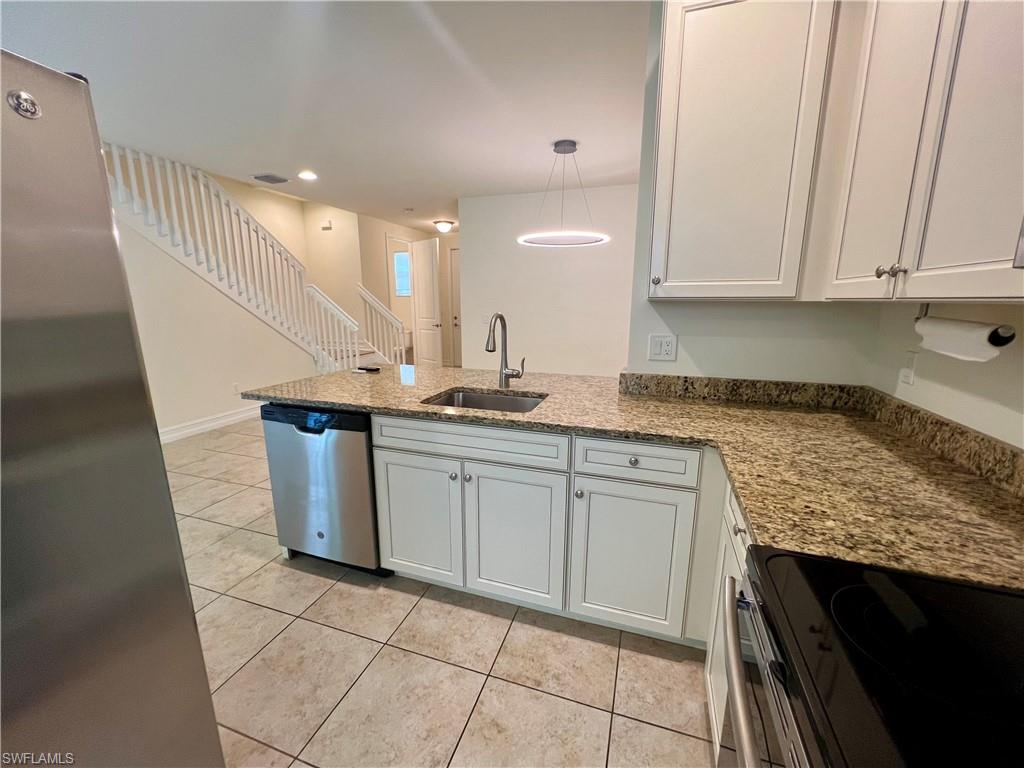Kitchen with decorative light fixtures, stainless steel dishwasher, white cabinetry, range, and light tile patterned floors