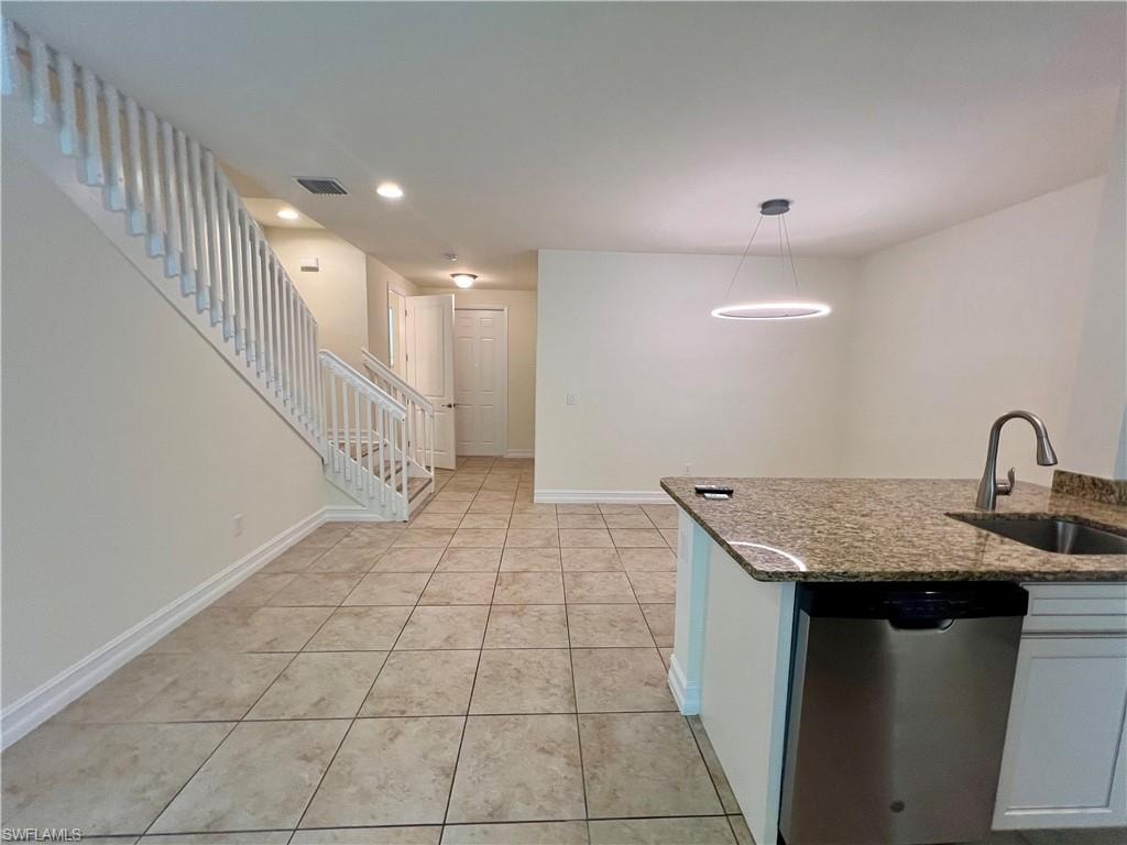 Kitchen with dark stone countertops, light tile patterned floors, stainless steel dishwasher, hanging light fixtures, and sink