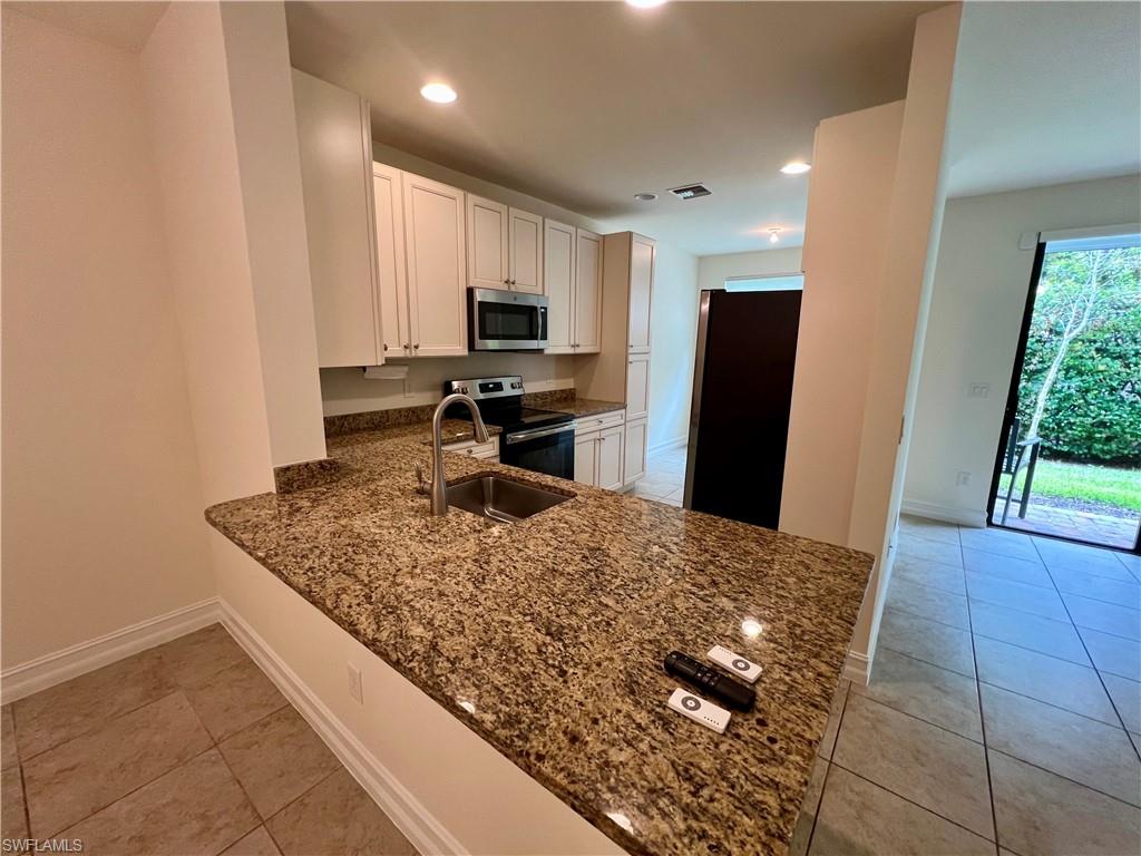 Kitchen with appliances with stainless steel finishes, dark stone counters, sink, light tile patterned flooring, and white cabinetry