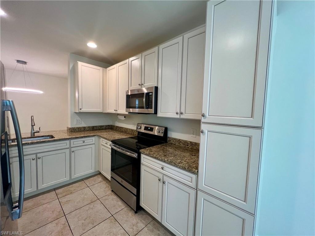 Kitchen with dark stone countertops, light tile patterned floors, white cabinets, appliances with stainless steel finishes, and sink