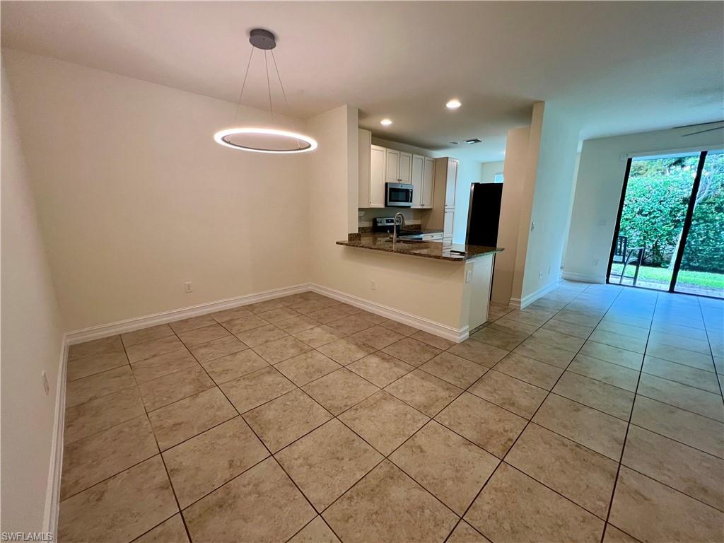 Kitchen featuring light tile patterned floors, kitchen peninsula, white cabinets, decorative light fixtures, and sink