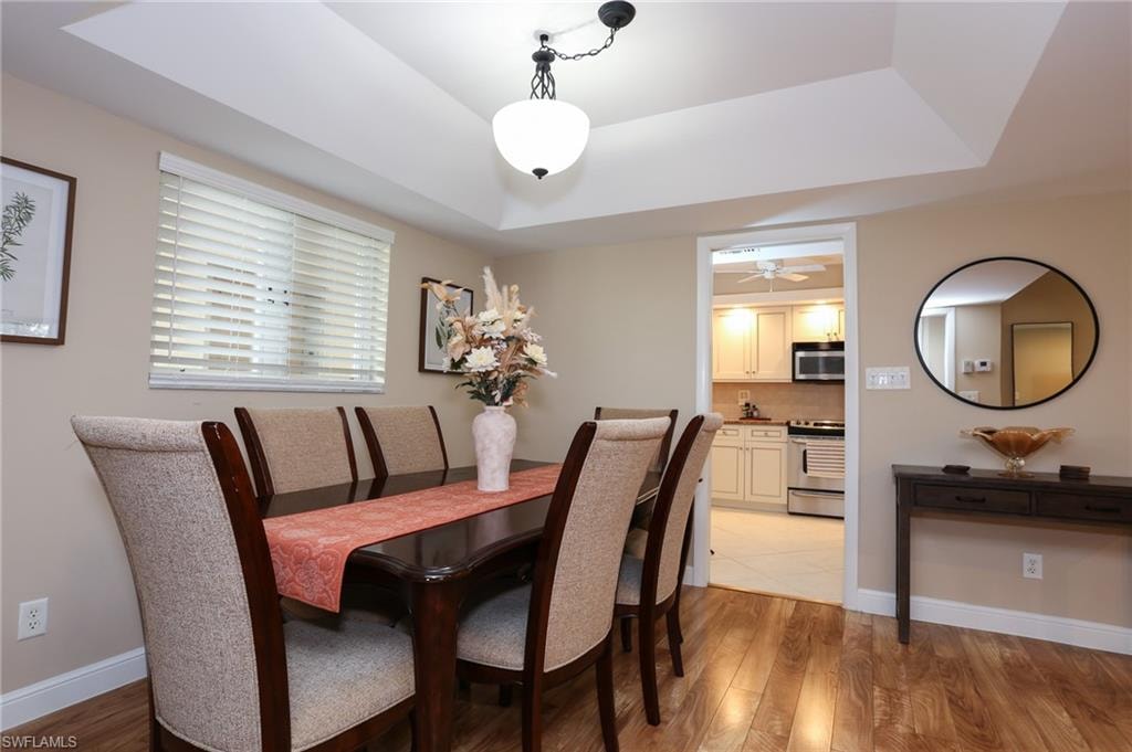 Dining space with light wood finished floors, baseboards, a ceiling fan, and a tray ceiling