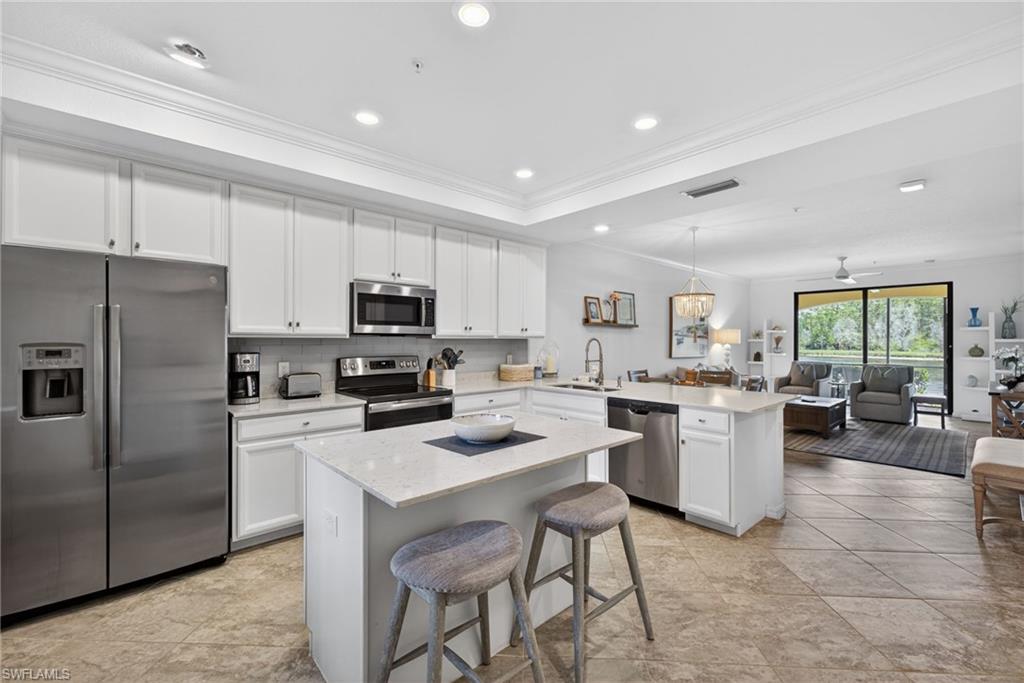 Open-concept kitchen featuring white cabinetry, stainless steel appliances, and a central island with a solid surface countertop