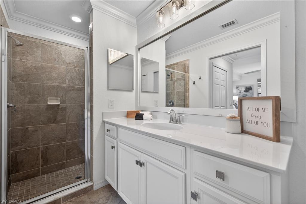 Bathroom featuring a spacious walk-in shower with tiled walls and floor, a single vanity with a white countertop, and a large wall-mounted mirror