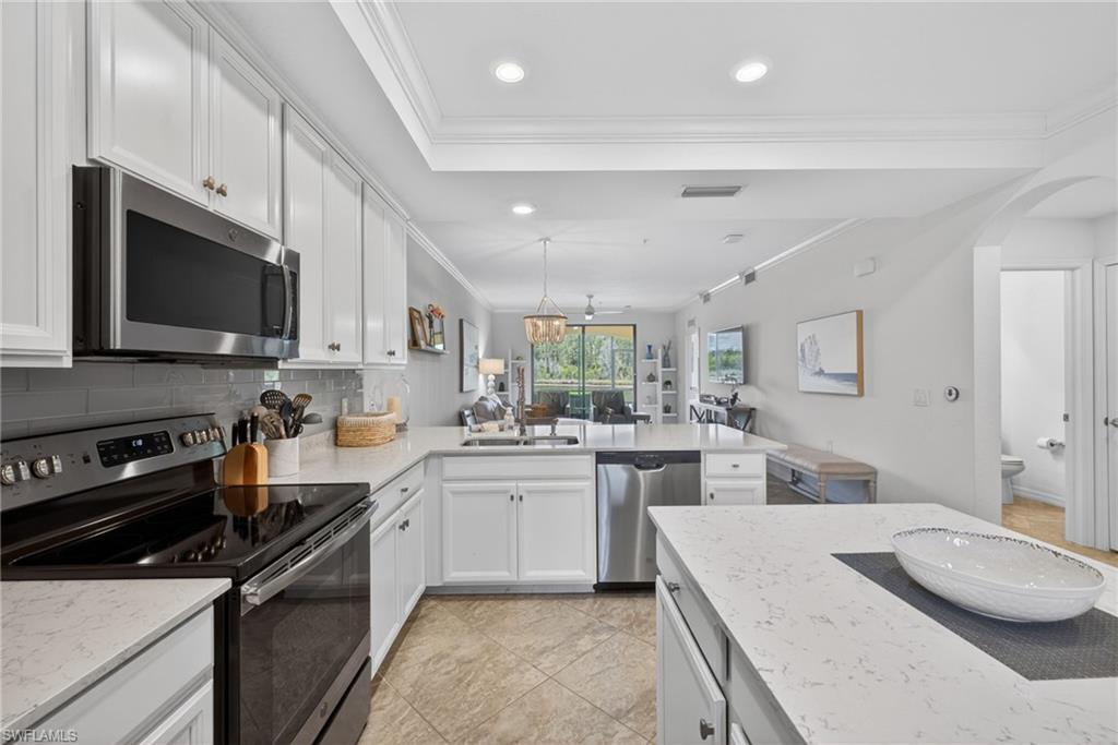 Kitchen featuring white cabinetry, stainless steel appliances, light-toned countertops, and a gray subway tile backsplash