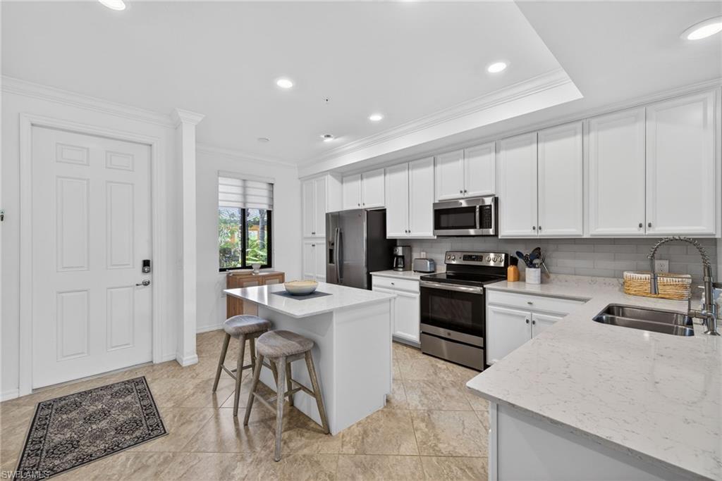 Modern kitchen featuring a central island, white shaker cabinetry, stainless steel appliances, light-toned countertops, and a subway tile backsplash