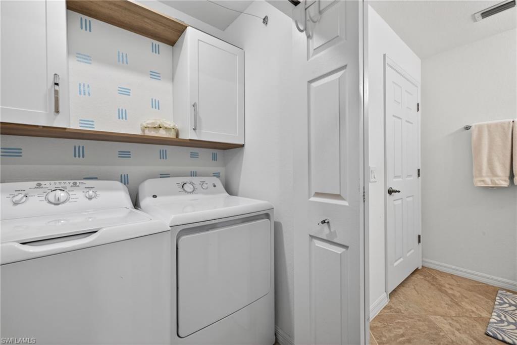 Laundry area featuring a side-by-side washer and dryer, wood-finish shelving, and white upper cabinetry with brushed nickel hardware