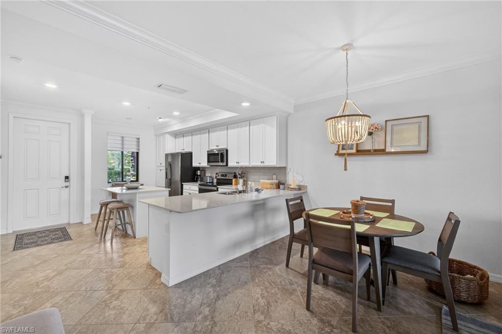 Open concept kitchen and dining area featuring white cabinetry, light-toned countertops, stone-look tile flooring, and a decorative chandelier