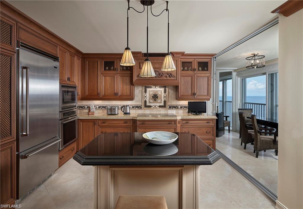 Kitchen with light tile patterned floors, light stone counters, built in appliances, decorative backsplash, and decorative light fixtures