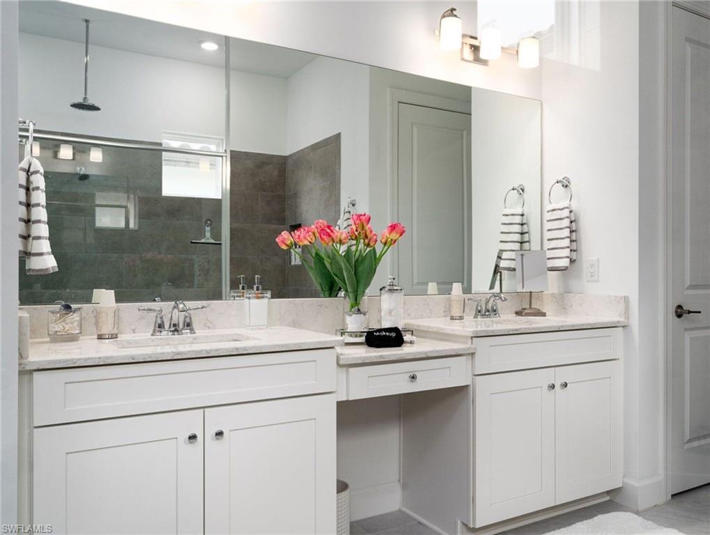 Spacious bathroom featuring a dual vanity with light-toned countertops, white cabinetry, a large wall-mounted mirror, a shower with dark gray tile surround, and a ceiling-mounted rainfall showerhead