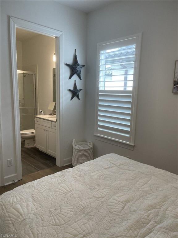 Room featuring a white bedspread, a window with white louvered shutters, and an adjacent bathroom entry