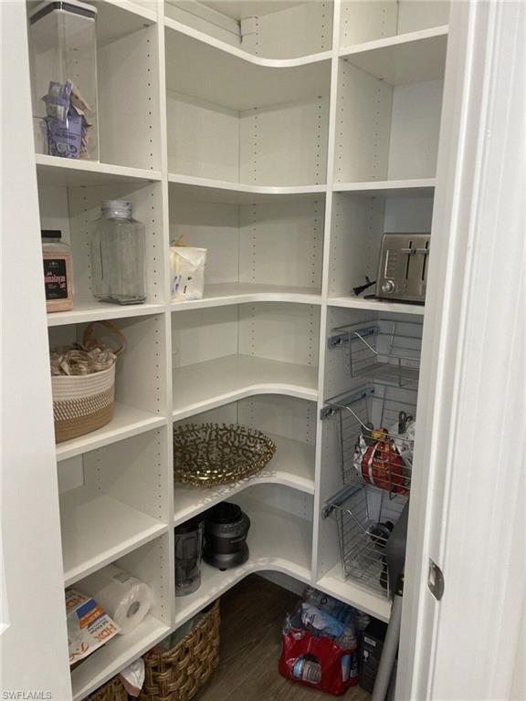 Walk-in pantry featuring white shelving, adjustable shelf heights, curved corner shelving, pull-out wire baskets, and wood-finish flooring