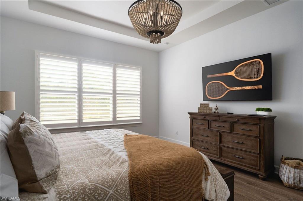 Tray ceiling with a decorative chandelier, multi-pane window with plantation shutters, wood-finish flooring, and light-toned wall paint