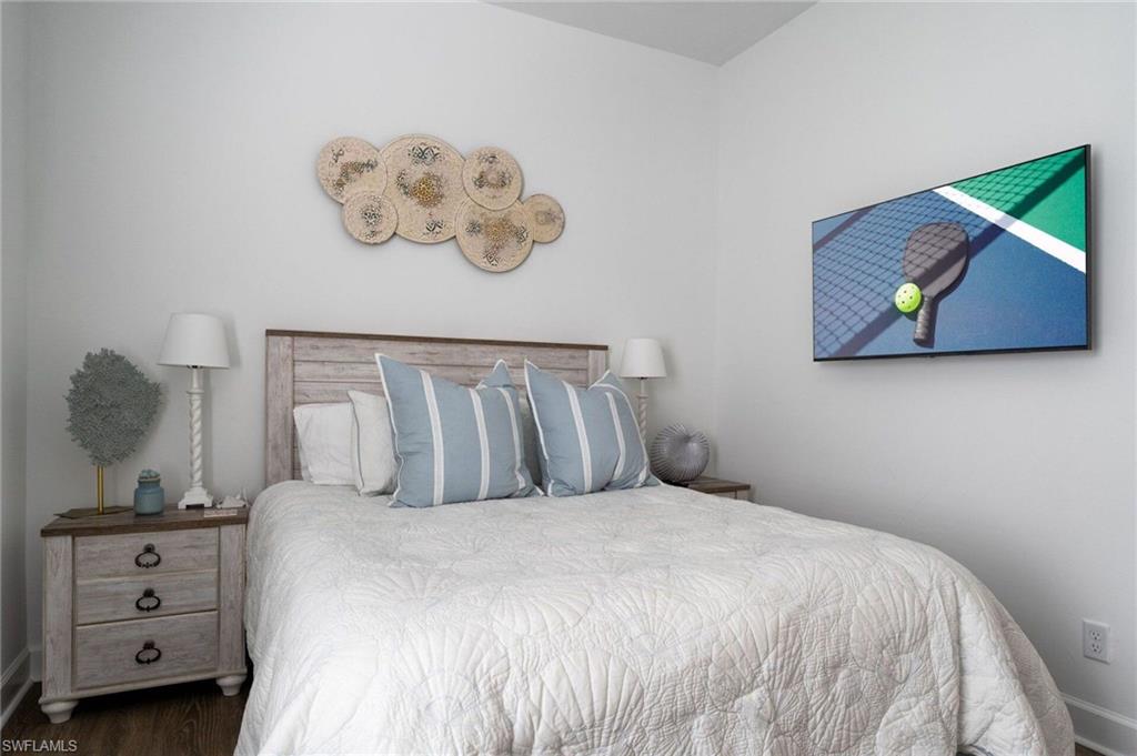 Bedroom featuring a distressed wood-finish headboard, wood-finish flooring, and a wall-mounted flat-screen television
