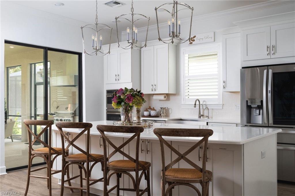 Bright kitchen featuring a white island with a light-toned countertop, white cabinetry with silver hardware, recessed lighting, and two ornate pendant light fixtures