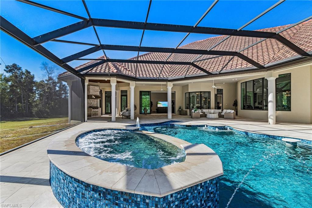 Screened outdoor living area featuring a tile roof, an integrated spa, and an expansive pool with water features