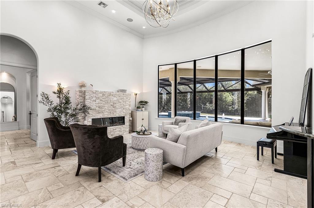 Spacious living area featuring high ceilings, a stone-clad fireplace, large format tile flooring, and an expansive curved window overlooking a screened pool enclosure and lush trees