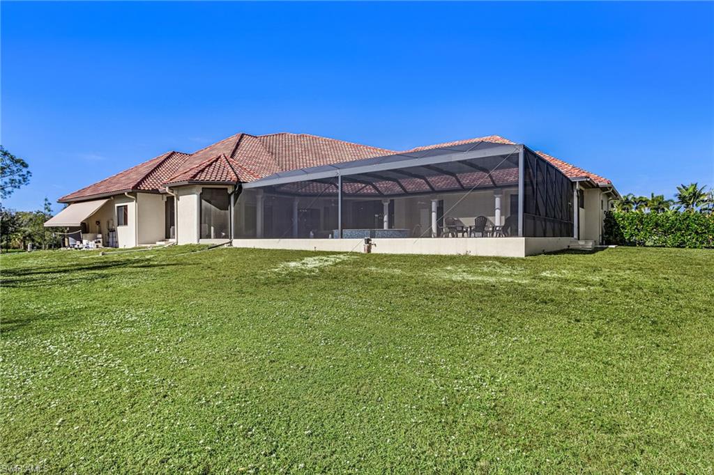 Expansive exterior featuring a screened-in lanai with structural columns, a red tile roof, and a beige stucco finish