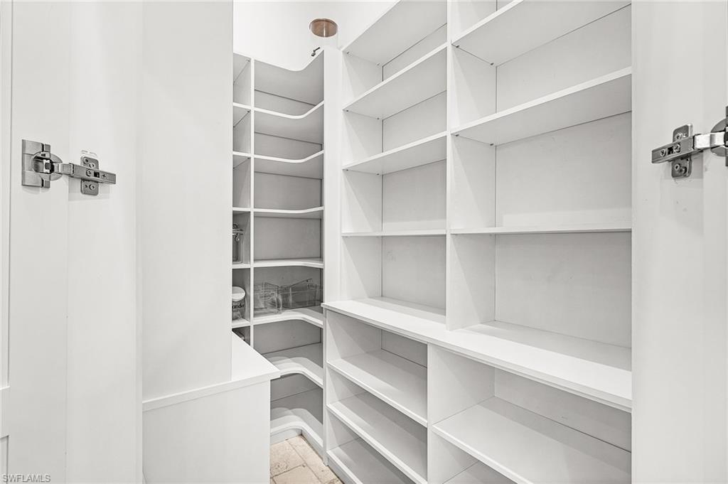 Walk-in pantry featuring extensive white shelving, corner shelving, and tile flooring