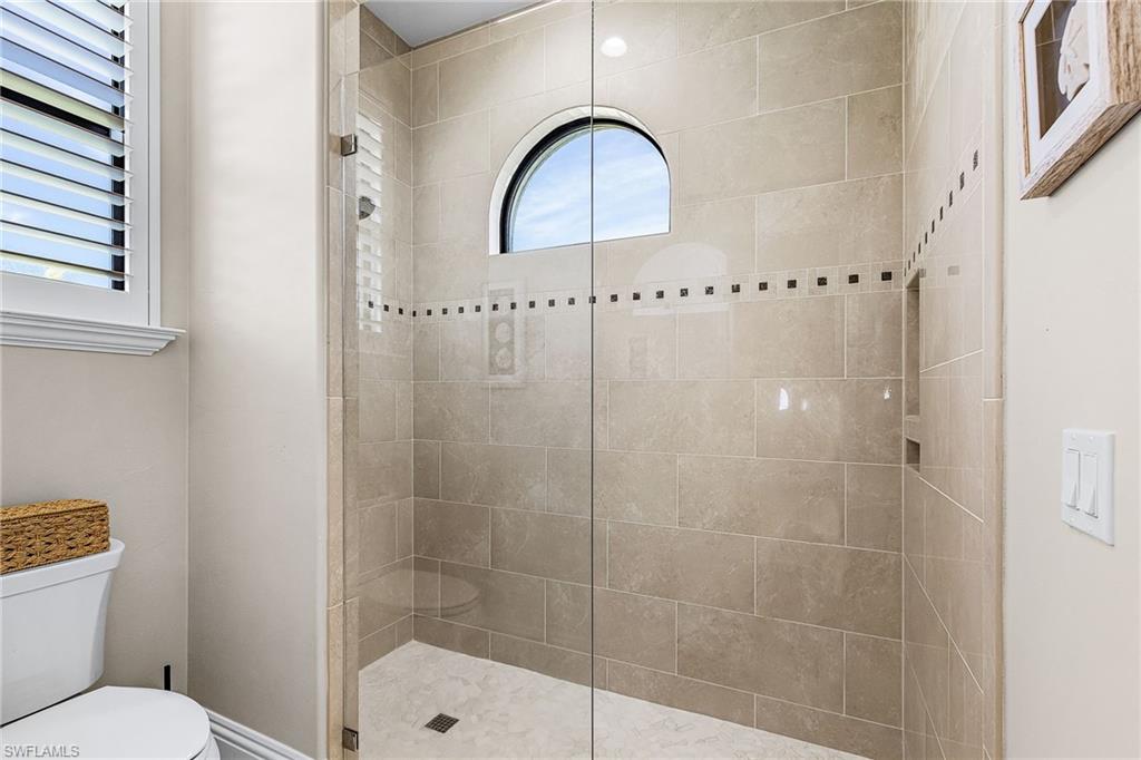 Glass-enclosed shower featuring large format tile, an arched window, and a recessed niche