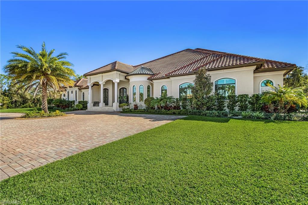 Mediterranean-style residence featuring a tile roof, stucco exterior, arched windows, and a paved circular driveway
