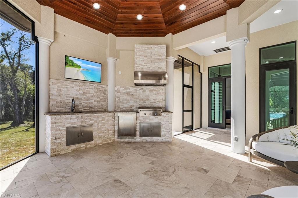 Expansive outdoor kitchen featuring stone veneer cabinetry, stainless steel appliances, a built-in sink, and a mounted television