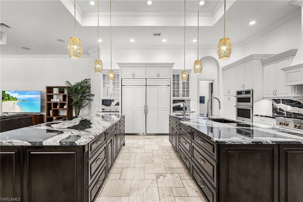 Gourmet kitchen featuring two expansive islands with stone countertops, a double-door built-in refrigerator, white cabinetry, and recessed lighting