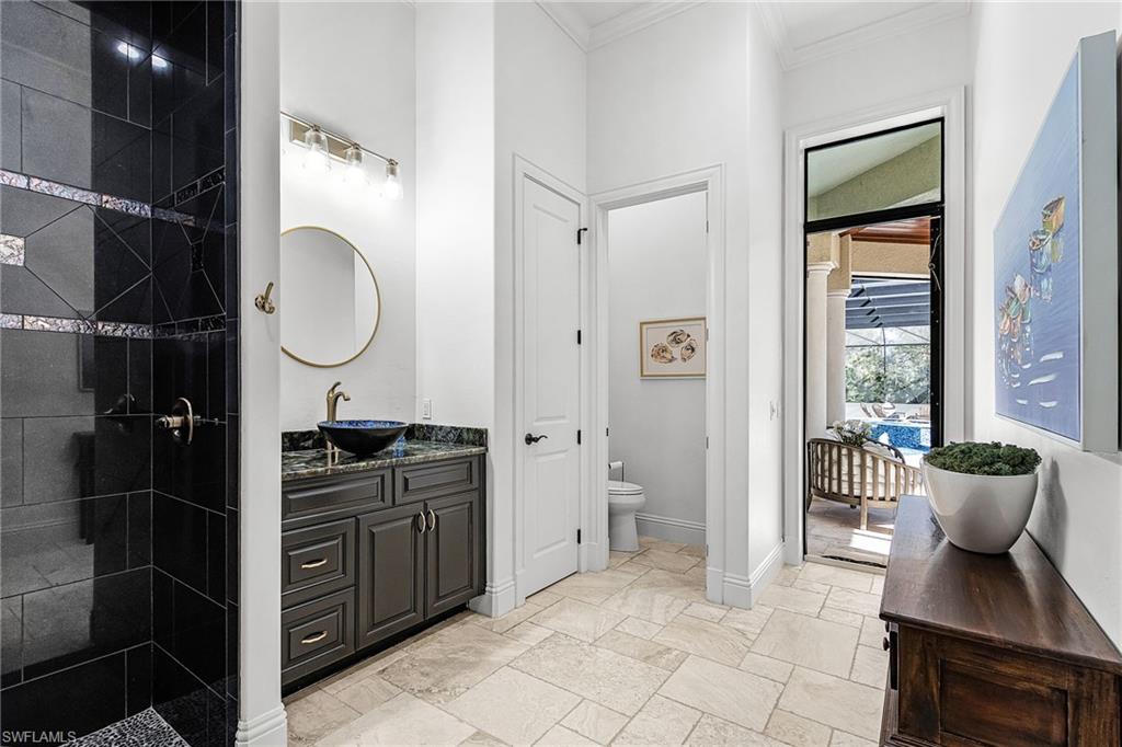 Contemporary bathroom featuring a dark tile shower with decorative accent bands, a vanity with a dark countertop and vessel sink, a gold-framed circular mirror, and light-toned tile flooring, perfect pool bath