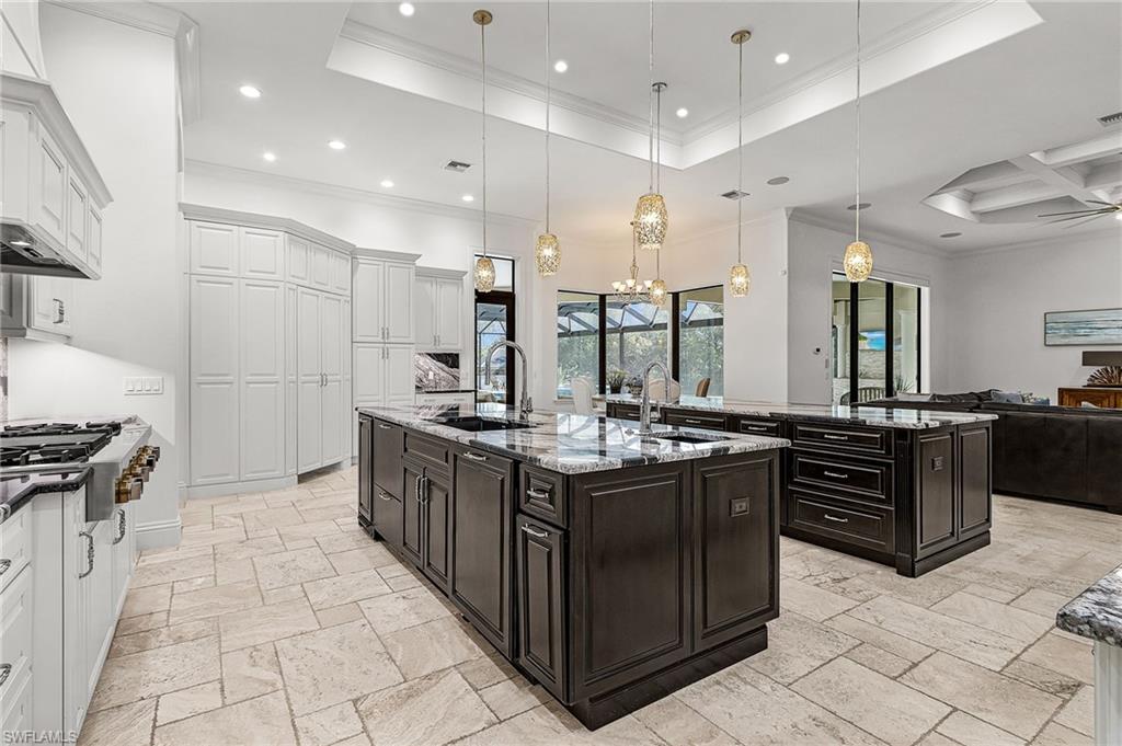 Spacious kitchen featuring two dark-toned islands with granite countertops, light-toned tile flooring, and white cabinetry