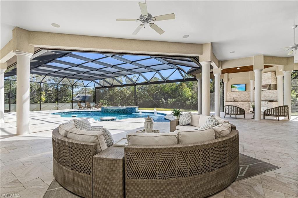 Screened-in outdoor living space featuring a large swimming pool with integrated spa and water features, extensive tiled decking, a built-in entertainment area with an overhead television, and structural columns