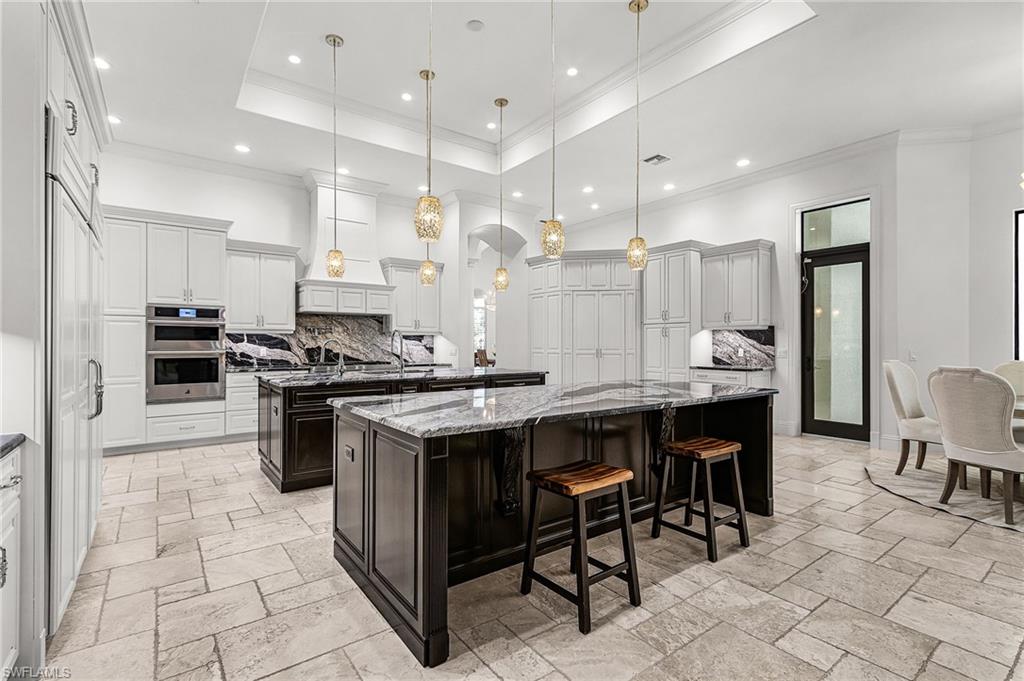 Gourmet kitchen featuring dual islands with stone countertops, a full suite of stainless steel appliances, extensive white cabinetry, and large format floor tile