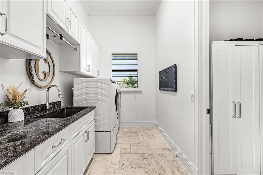 Laundry room featuring white cabinetry, a dark stone countertop with an integrated sink, chrome fixtures, and light-toned tile flooring