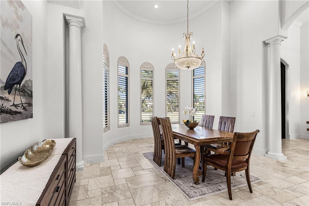 Spacious room featuring a tray ceiling, arched windows with plantation shutters, decorative columns, and tile flooring